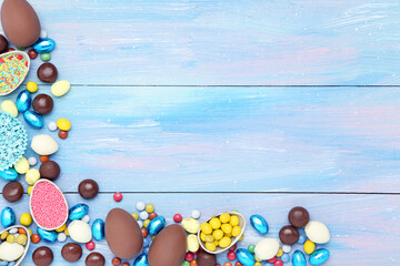 Wall Mural - Easter chocolate eggs with candies and sprinkles on blue wooden table