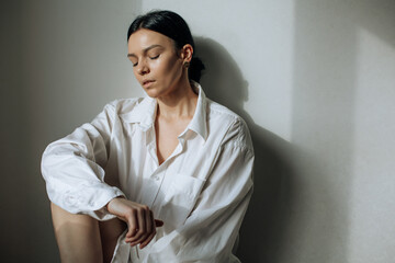 Poster - Beautiful young brunette sitting in a white shirt under the rays of the sun with closed eyes. Horizontal photo