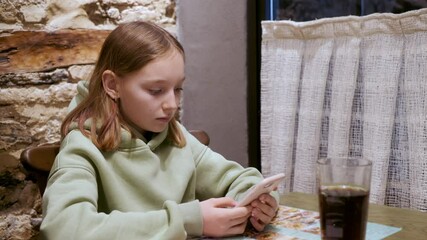 teenager girl using mobile phone at table with paper menu in cafe. young girl browsing smartphone wi