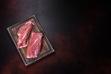 Raw duck breast with herbs and spices on a dark concrete background