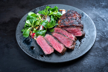 Modern style traditional dry aged sliced wagyu roast beef with corn salad and pine nuts served as close-up on a Nordic design plate