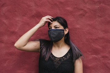 Young Ecuadorian female with a fabric face mask on burgundy wall background