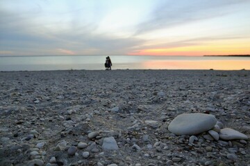 Silhouettes of people walking along the pebble beach of the lake.  Beautiful sunset in the background.