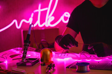 Wall Mural - Cropped view of man holding wires of glowing neon near tools in workshop 