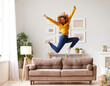 © JenkoAtaman - Happy african american teen girl jumping on sofa while having fun on weekend at home