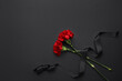 Black funeral ribbon with carnation flowers on dark background