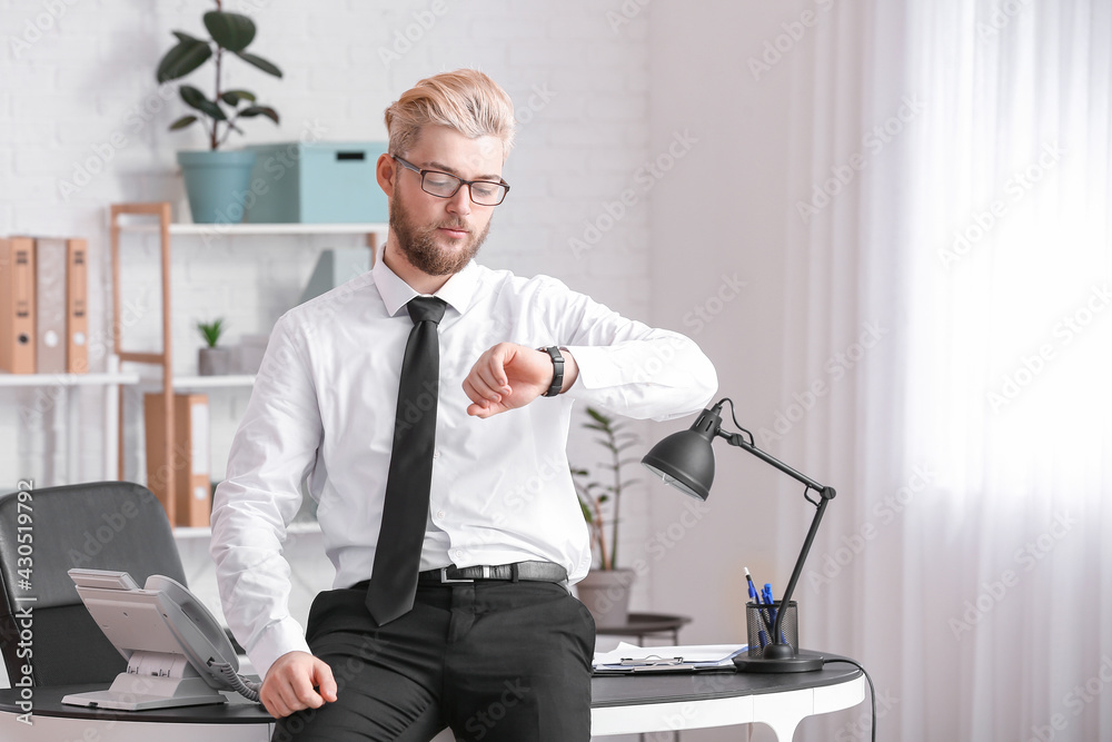 Young man looking at wristwatch in office