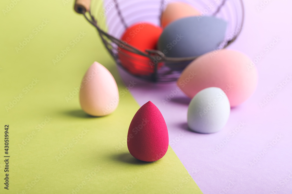 Overturned basket with makeup sponges on color background
