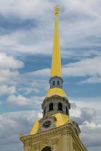 The Upper Part Of The Peter And Paul Cathedral In St. Petersburg (Russia). A Yellow Spire With An Angel, A Clock, A Sculpture And Turrets Are Shown On A Large Scale. Blue Sky With White Clouds 