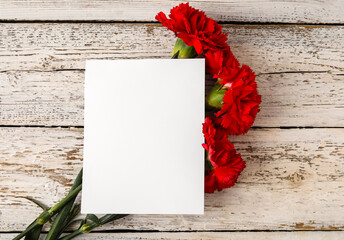 Fresh carnation flowers with empty paper sheet on white wooden background