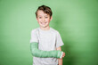 © epiximages - cool young schoolboy with broken arm and green plaster posing in front of green background in the studio
