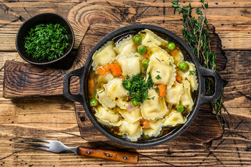 Wall Mural - Broth soup with ravioli dumplings pasta in a pan. Wooden background. Top view