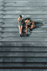 Wall Mural - Athletic couple sitting on concrete staircase after jogging or fitness workout outdoors