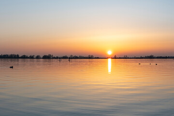 Wall Mural - Two persons on paddleboards paddle their way home during a sunset at lake Zoetermeerse Plas, the Netherlands