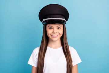 Poster - Photo of happy cheerful smiling positive little girl wear pilot cap and white t-shirt isolated on blue color background