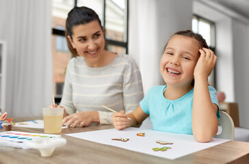 Poster - family, motherhood and leisure concept - happy smiling mother spending time with her little daughter drawing or painting wooden chipboard items with colors at home