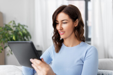 people, technology and leisure concept - happy young woman with tablet pc computer at home