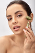 © Peakstock - Facial jade roller. Young woman massages her sensuality face using a green jade massager roller for elastic perfect skin