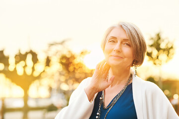 Outdoor portrait of beautiful and elegant mature woman posing in sunlight