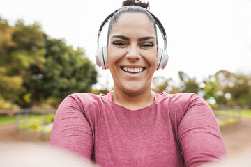 Curvy young woman taking selfie with smartphone while doing jogging routine outdoor at city park - Plus size and sport workout exercises concept