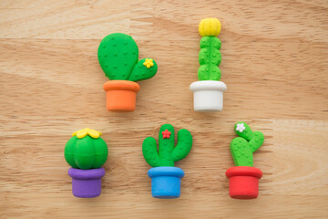 Flat lay of cute cactus in color pot toy eraser set on wooden background minimal style. Kid learning, development, love plant and funny play by small eraser toy in school accessories.