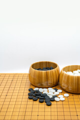 Isolated traditional board game of China and Japan, called Go, two opened wooden bowls of black stones and white stones. The vertical image on white background.