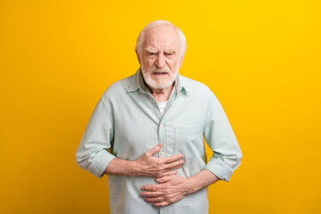 Wall Mural - Photo of upset stressed mature man dressed green shirt arms stomach feeling pain isolated yellow color background