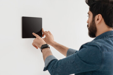 Poster - Innovative technology for apartment. Guy using digital tablet on wall with smart home control system app