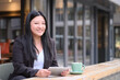 © Robert - portrait of smiling Asian young business woman using digital tablet at outdoor cafe, looking at camera