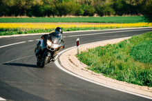 Motorcycle Driver Riding Alone On The Asphalt Road. Lifestyle Photo Of A Biker In The Motion At The Empty Road