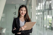© amnaj - Image of a beautiful young Asian businesswoman stand at the modern office. Looking at the camera.