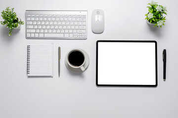 Top view white desk with tablet blank white screen coffee keyboard mouse notebook On a white table. Mockup.