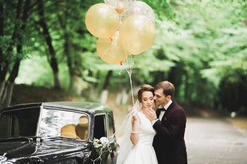 Beautiful newlywed couple posing near retro black car