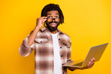 Photo portrait of amazed brunet man touching glasses working on computer smiling isolated on bright yellow color background