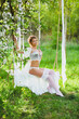 Young bride with blond hair in white negligee and stockings sitting on a rope swing