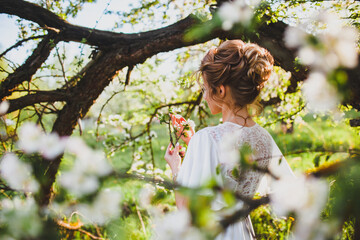 Young bride with blond hair posing at the background of spring orchard