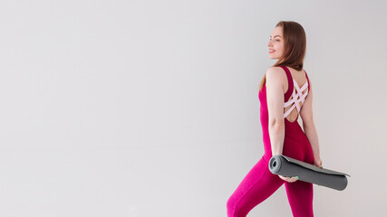 Beautifull young blond sportswoman holding yoga or fitness mat isolated over grey background. Healthy life, keep fit concepts.