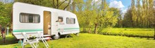 White Caravan Trailer On A Green Lawn In A Camping Site. Sunny Day. Spring Landscape. Europe. Lifestyle, Travel, Ecotourism, Road Trip, Journey, Vacations, Recreation, Transportation, RV, Motorhome