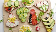 Vegetarian fresh sandwiches on a wooden cutting board. Vegetable fillings and herbs. View from above. Top view. Rotation.