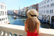 Holidays in Venice. Back view of beautiful girl in red dress enjoying view of Grand Canal from Rialto Bridge in Venice, Italy.