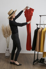 Wall Mural - Beautiful young woman near rack with clothes holding long terracotta dress.