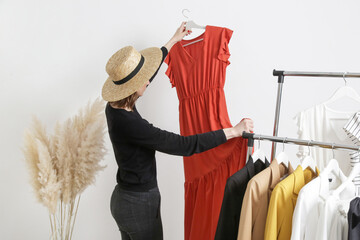 Wall Mural - Beautiful young woman near rack with clothes holding long terracotta dress.