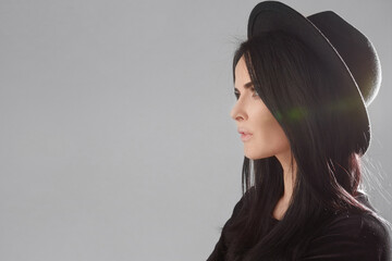 Wall Mural - Close-up side view of a young model woman in a black hat isolated at the white background