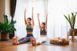 © chayantorn - Asian young mother teaching her daughter to yoga pose and exercise together with their dog on yoga mat in living room at home.
