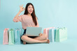 © Songkhla Studio - Online Order. Asian girl sitting with laptop using credit card shopping online on blue background, shopping online concept