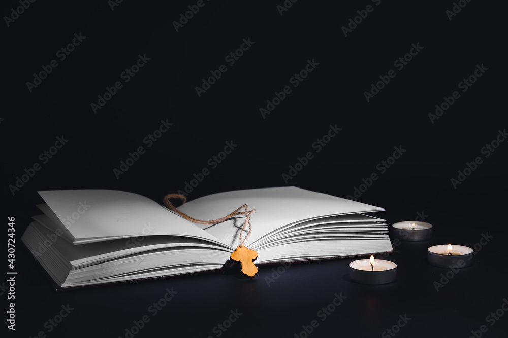 Wooden cross with book and candles on dark background