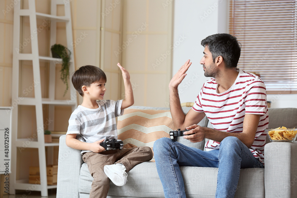 Father and little son playing video games at home