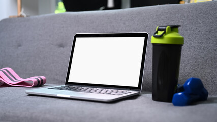 Mock up computer laptop with blank screen, bottle of water and dumbbells on sofa