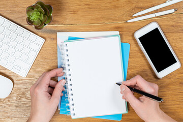 Workspace with a keyboard, girl's hands writes in a notebook on a wooden table, top view of an office desk table. Freelancer's place of work