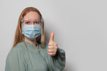 Woman wearing protective mask and face shields holding thumb up. Covid-19 protection concept